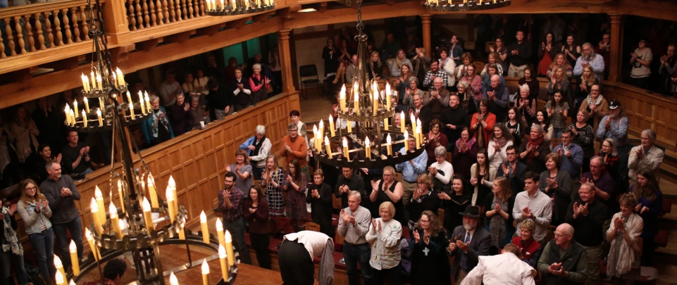 A crowd within the Blackfriar's Playhouse gives standing ovation to performers on stage.